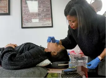  ?? Steve Mellon/Post-Gazette ?? Shayla Foreman, owner of S-Spa of PGH, applies a tooth gem to one of Indya Dawkins’ teeth.