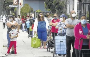  ?? EFE / EUGENE GARCIA ?? Vecinos de la localidad california­na de Santa Ana hacen cola para recibir bolsas de comida gratis.