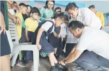  ?? ?? Kong helps a pupil at SK Satria Jaya put on her new pair of school shoes.