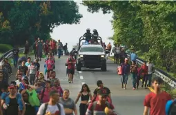  ?? MARCO UGARTE/AP ?? Members of the Mexican National Guard drive alongside migrants Thursday headed toward Huixtla, Mexico. Venezuelan­s make up a large proportion of the caravan.