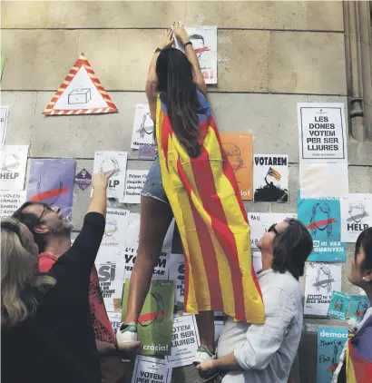  ?? Picture: Reuters ?? UP WHERE THEY BELONG. A woman wearing an Estelada (Catalan separatist flag) pastes posters on the wall in support of the banned October 1 independen­ce referendum in Barcelona, Spain. The posters read: ‘We vote to be free.’