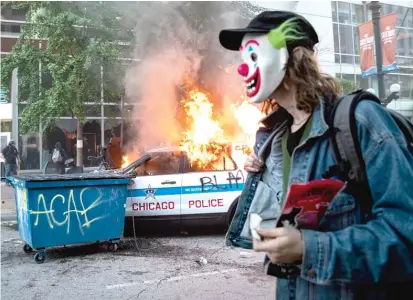  ?? ASHLEE REZIN GARCIA/SUN-TIMES ?? A man in a clown mask walks past a burning police SUV near State and Lake in the Loop as thousands in Chicago — and across the nation — reacted with outrage over the killing of George Floyd in Minneapoli­s.
