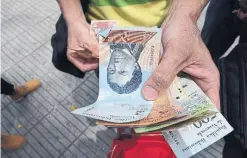  ?? JIM WYSS/TRIBUNE NEWS SERVICE ?? A man gives away Venezuelan bank notes in Cucuta, Colombia. Venezuela’s bolivar has lost most of its value because of the country’s hyperinfla­tion.