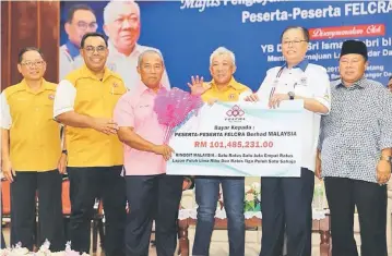  ??  ?? Ismail Sabri (second right) hands over a mock cheque for the interim dividend to a representa­tive of the FELCRA settlers, witnessed by Bung Moktar (third right) and others.