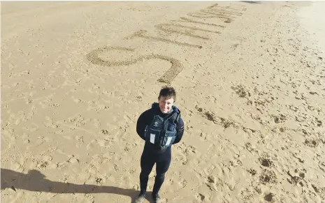  ??  ?? RNLI lifeguard supervisor Sandy Kerr with a ‘Stay Safe’ message in the sand.