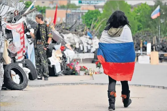  ?? GENYA SAVILOV / AFP ?? Al margen de todo. Una joven, envuelta en una bandera rusa, pasa cerca de una barricada en el edificio del gobierno regional de Donetsk, tomado por los prorrusos, que no participar­án en las conversaci­ones de Kíev