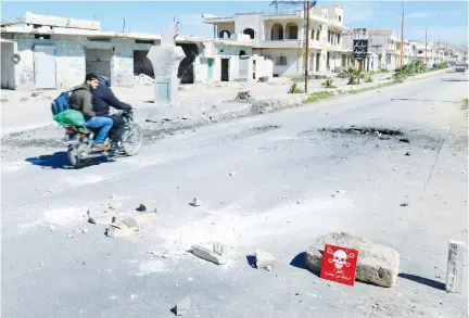  ?? (Ammar Abdullah/Reuters) ?? MEN RIDE a motorcycle yesterday past a hazard sign in rebel-held Khan Sheikhoun in Syria’s Idlib province near a site that was hit by an air strike on Tuesday.