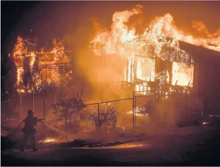  ??  ?? > A firefighte­r sprays water as flames from a wildfire consume a residence near Oroville, California, yesterday