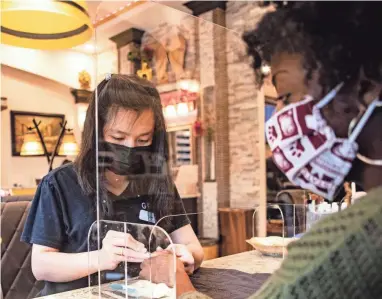  ?? ARIEL COBBERT/THE COMMERCIAL APPEAL ?? A nail salon employee works on a customer through a plexiglass shield at Gloss Nail Bar in Memphis on Tuesday as businesses reopened after closures forced by COVID-19.