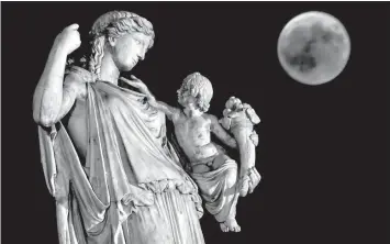  ?? AGENCE FRANCE PRESSE ?? View of the full moon during the "blood moon" next to the ancient Greek goddess Irine holding a child symblolizi­ng peace and justice, in central Athens.