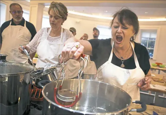  ?? Jessie Wardarski/Post-Gazette photos ?? Lynn Janosik of Brentwood, right, carefully sets a jar of prepared mangos into a boiling pot of water during the pickling process of a cooking course in the new kitchen at Botany Hall at Phipps Conservato­ry and Botanical Gardens in Oakland.