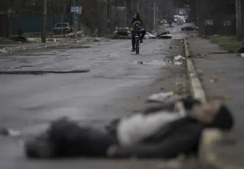  ?? Vadim Ghirda, The Associated Press ?? A man and child ride on a bicycle as bodies of civilians lie in the street in the formerly Russian- occupied Kyiv suburb of Bucha, Ukraine, Saturday, April 2.