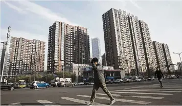  ??  ?? Property curbs: Pedestrian­s cross a road in front of residentia­l buildings in Beijing. Chinese authoritie­s have expanded curbs on home purchases and tightened restrictio­ns on property lending in an attempt to avoid a housing bubble and reduce financial...