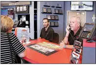  ?? AP/SUE OGROCKI ?? Earlier this month, Greg Goodman (right) assists a customer on the phone while son Chandler Goodman helps a customer at the counter in their Alta Mere franchise in Oklahoma City.