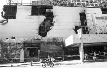  ?? — AFP photo ?? A man cycles past the Waterfront Manila Pavilion hotel in Manila a day after the hotel and casino complex was hit by fire.