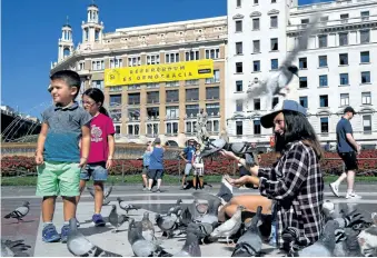  ?? AFP/GETTY IMAGES ?? A woman and some children feed pigeons Wednesday in Barcelona’s Catalonia square in front of a building with a banner reading “Yes. Referendum is democracy” calling to vote in the October 1 referendum on Catalan independen­ce.