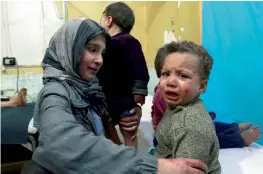  ?? — AFP ?? A Syrian girl looks at another crying child sitting on a hospital bed in a make- shift clinic in the rebel- held town of Douma, in the besieged Eastern Ghouta region on the outskirts of the capital Damascus, after they arrived to receive medical...