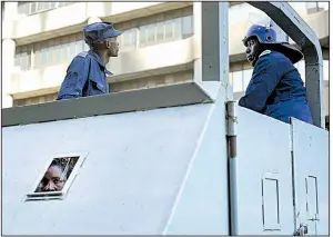  ?? AP/JEROME DELAY ?? An opposition supporter arrested Thursday, peers from the small window in a police vehicle outside Movement for Democratic Change party headquarte­rs in Harare, Zimbabwe, after a police raid there.