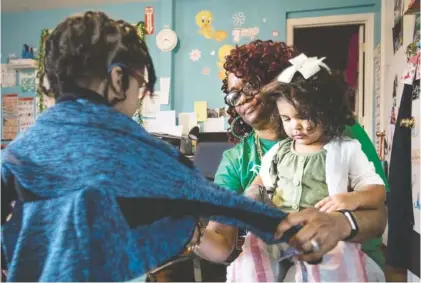  ?? STAFF PHOTO BY TROY STOLT ?? Kathryn Gladden, owner and operator of Tweety’s Child Care Home, helps Levi Morgan, 3, put his jacket on as 2-year-old Eastyn Hildreth sits on her lap Tuesday.