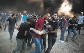  ?? Khalil Hamra / Associated Press ?? Palestinia­n protesters evacuate a man shot by Israeli troops at the Gaza Strip border. The Israeli military said 14,000 Palestinia­ns thronged the fence areas.
