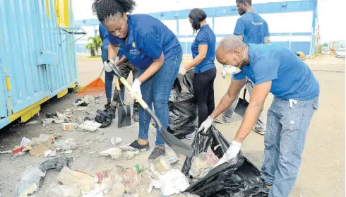  ??  ?? Kingston Wharves Limited staffers get under food trailers along the roadway to retrieve garbage as part of their clean-up exercise.