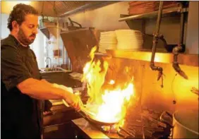  ??  ?? Flames rise from a pan as Chef Sean Weinberg cooks pork at his Restaurant Alba in Malvern.