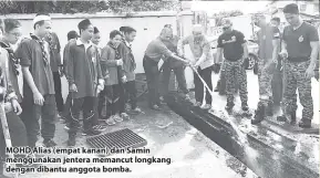  ??  ?? MOHD Alias (empat kanan) dan Samin menggunaka­n jentera memancut longkang dengan dibantu anggota bomba.