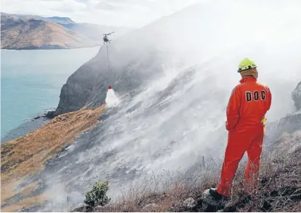  ?? Photo: JOHN KIRK-ANDERSON/FAIRFAX NZ ?? Heavy duty: ADepartmen­t of Conservati­on staffer looks on as a helicopter with a monsoon bucket attacks a fire at Godley Head.