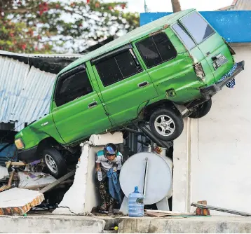  ?? JEWEL SAMAD/AFP/GETTY IMAGES ?? A survivor walks under a car struck on a building in Palu, on the Indonesian island of Sulawesi, on Monday, after an earthquake and tsunami hit the area on Friday, killing more than 840 people.