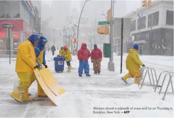  ?? — AFP ?? Workers shovel a sidewalk of snow and ice on Thursday in Brooklyn, New York.