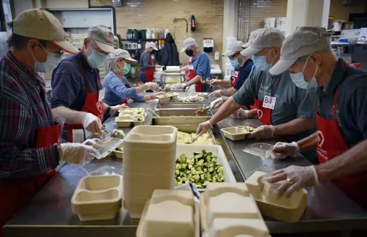  ?? Photos by Eric Lutzens, The Denver Post ?? Project Angel Heart volunteers assemble plates of Moroccan-braised chicken, couscous and zucchini in the nonprofit’s kitchen on Thursday.