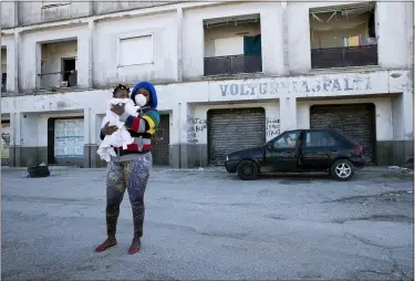  ?? ALESSANDRA TARANTINO — THE ASSOCIATED PRESS ?? A woman wearing a sanitary mask to protect against COVID-19holds her daughter as she walks past a building April 27 in Castel Volturno, near Naples, Southern Italy.
