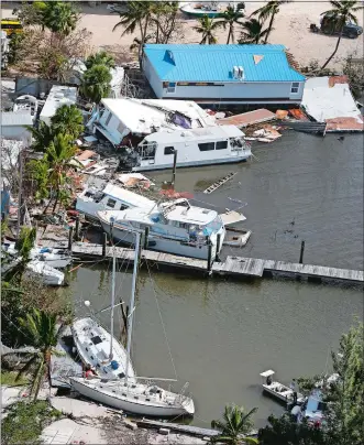  ?? AP PHOTOS ?? boats and buildings are damaged in Key Largo. Above left, a house slides into the ocean in Ponte Vedra Beach. Above right, Larry Dimas walks around the remains of his trailer in Immokalee. His tenants evacuated and nobody was inside when it was...