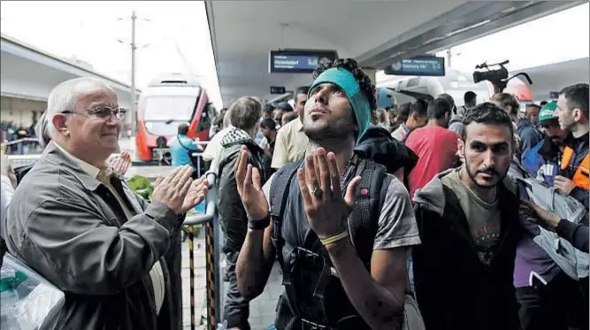  ?? ALEX DOMANSKI / GETTY ?? Un joven migrante eleva una oración de agradecimi­ento mientras un ciudadano austriaco aplaude, ayer en la estación de Viena