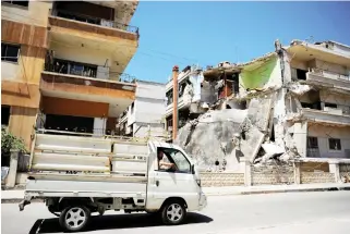  ??  ?? A truck passes a damaged building in Waer district in the central Syrian city of Homs. (Reuters)