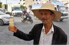  ??  ?? A street vendor holds a bottle of legmi, a coveted date palm drink, in the southweste­rn Tunisian town of Gabes.