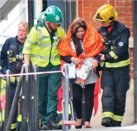  ??  ?? Barefoot blast victim: A distressed woman wearing only one shoe is led away from the station by rescuers