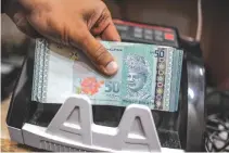  ??  ?? A MONEY CHANGER counts Malaysian ringgit banknotes for customers in Kuala Lumpur.