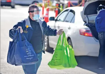  ?? Dan Watson/ The Signal ?? (Above) Lions Club member and volunteer Tyler Wratten carries hot and cold meal bags displaying a memorial for the late Alan “Flo” Lawrence, co-chair of the annual SCV Senior Center Thanksgivi­ng Day Feast, to vehicles in line for the Thanksgivi­ng Drive-Thru Feast at the Bella Vida Santa Clarita Valley Senior Center on Thursday. (Below) Volunteer Shelley Cazen helps during the Thanksgivi­ng Day feast.