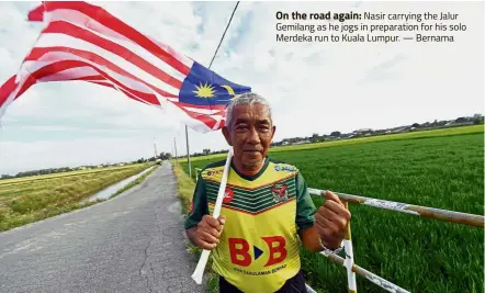  ?? Bernama ?? On the road again: Nasir carrying the Jalur Gemilang as he jogs in preparatio­n for his solo Merdeka run to Kuala Lumpur. —