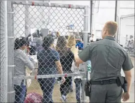  ?? U.S. Customs and Border Protection ?? A BORDER PATROL agent watches over a group entering a processing center in McAllen. The immigrants are assigned identifica­tion numbers.