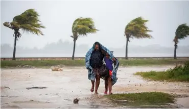  ?? ASSOCIATED PRESS PHOTOS ?? A woman and child use a blanket as protection from the wind and rain Friday as they walk in Caibarien, Cuba.