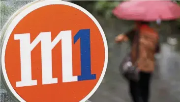  ??  ?? Valued asset: A woman with an umbrella passes an M1 sign in Singapore. Assuming that Axiata accepts the offer of S$2.06 a share, it could net a gain of about S$550mil or RM1.6bil. — Reuters