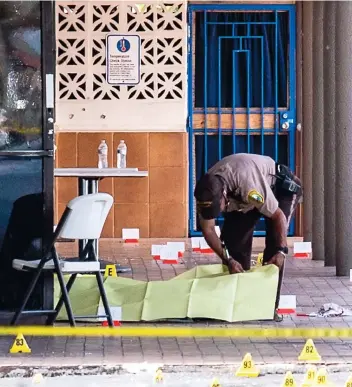  ?? PHOTO AFP ?? Un policier recouvre le corps d’une des victimes de la fusillade survenue devant la boîte de nuit El Mula Banquet Hall située sur l’artère Hialeah de Miami.