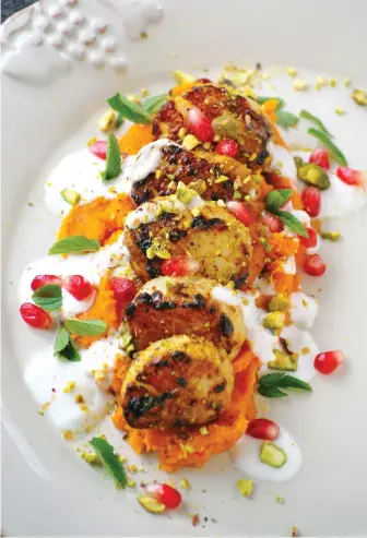  ??  ?? In this dish, succulent scallops are set on mashed yams and adorned with pistachios and pomegranat­e seeds.