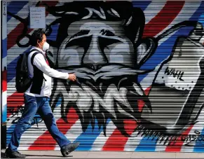  ??  ?? A man walks past graffiti-sprayed shutters of a closed barber shop in London last week. (AP/Frank Augstein)