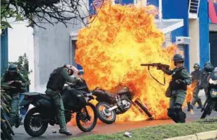  ??  ?? ... Venezuelan riot security forces clash with demonstrat­ors as a motorcycle is set on fire during a protest against President Nicolas Maduro’s government in San Cristobal on Monday.
