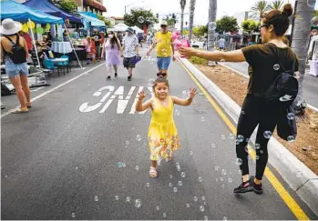  ?? ?? Elsie Carrillo used a bubble maker to entertain her daughter, Alexandra Perez, 4, as they head down Chula Vista’s Third Avenue during the Lemon Festival on Saturday.