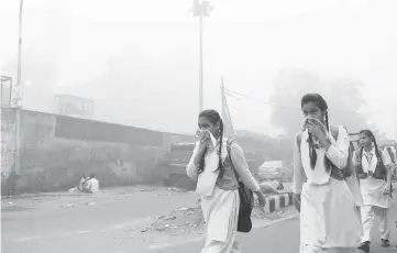  ?? — AFP photo ?? Indian schoolchil­dren cover their faces as they walk to school amid heavy smog in New Delhi.