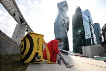  ??  ?? A Yandex courier uses his smartphone in front of skyscraper­s of Moskva City business centre in Moscow.